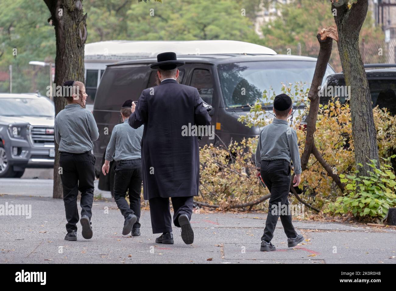Un padre judío ortodoxo y sus 3 niños vestidos de forma idéntica caminan en Williamsburg, Brooklyn en un suave día de finales del verano de 2022. Foto de stock