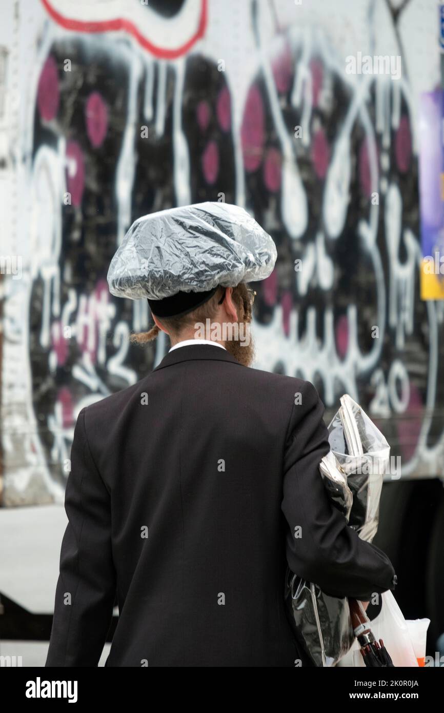 En un día de verano, un judío hasidico lleva un sombrero de lluvia de estilo inusual. En Lee Avenue en Williamsburg, Brooklyn, Nueva York. Foto de stock