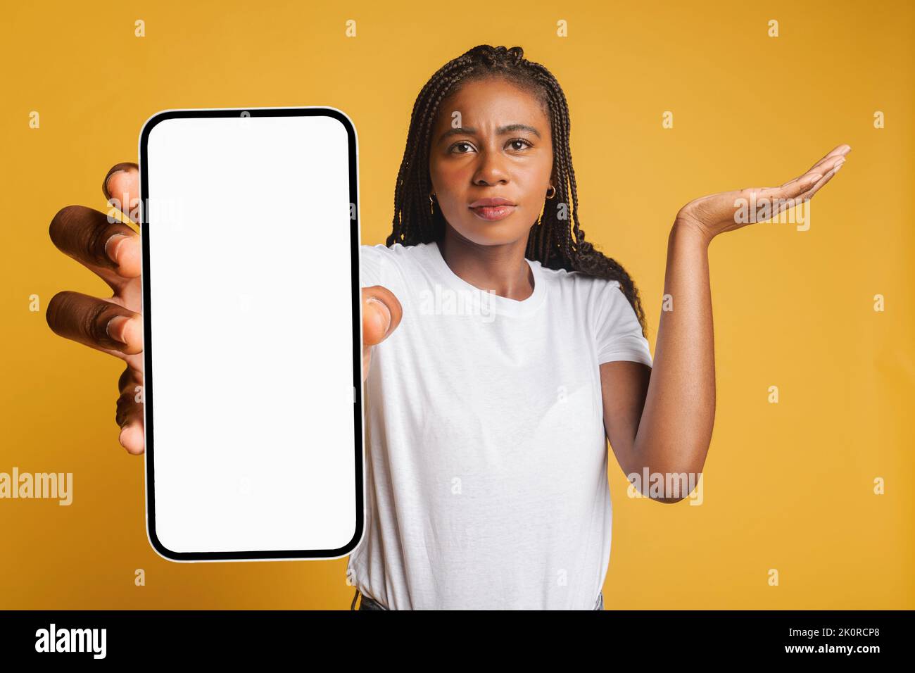 Una joven afro-americana decepcionada sosteniendo un smartphone y mirando la cámara, la señora recibió mala notificación o mensajes, se siente molesta, encogiéndose de hombros, aislada Foto de stock