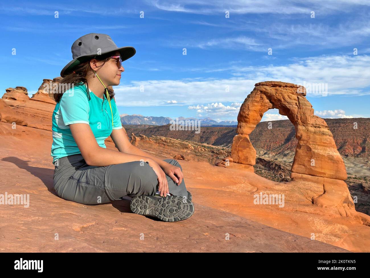 Joven turista sentada frente a Delicate Arch al atardecer en Utah, Estados Unidos Foto de stock