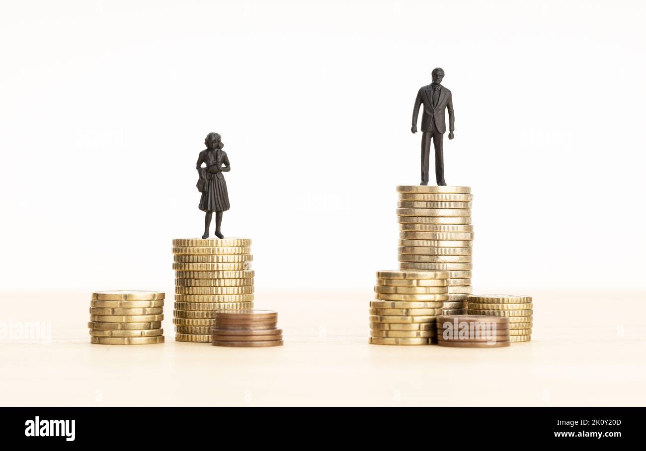Concepto de brecha salarial de género. Figurillas de hombre y mujer de pie sobre la pila de monedas. Espacio de copia Foto de stock