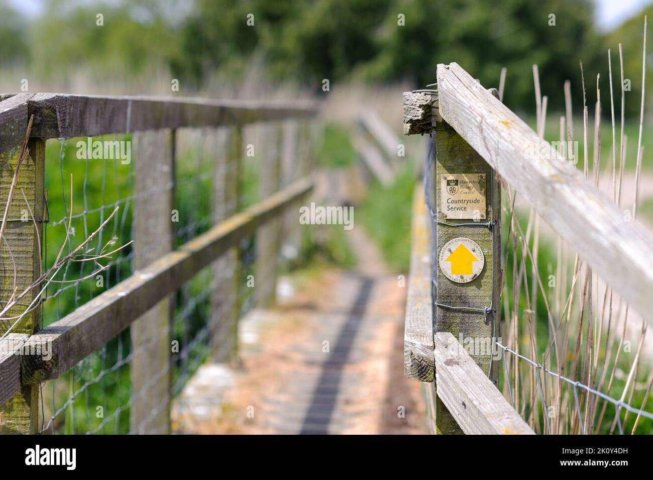 Señal de dirección de sendero de flecha amarilla en el poste de puente de madera, servicio rural, Hampshire, Reino Unido Foto de stock