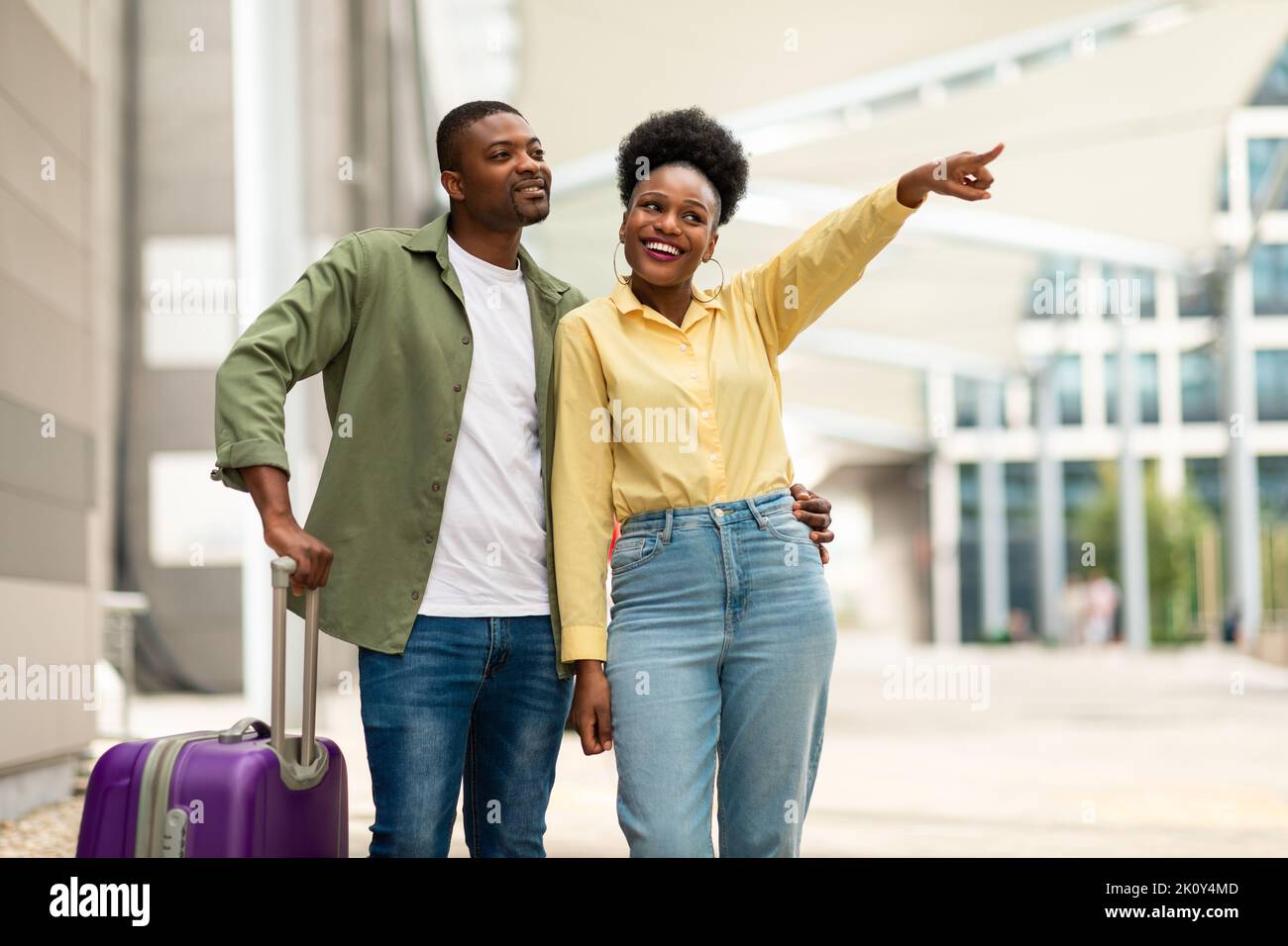 Una pareja de turistas negros con la maleta apuntando con el dedo a un lado en el aeropuerto Foto de stock