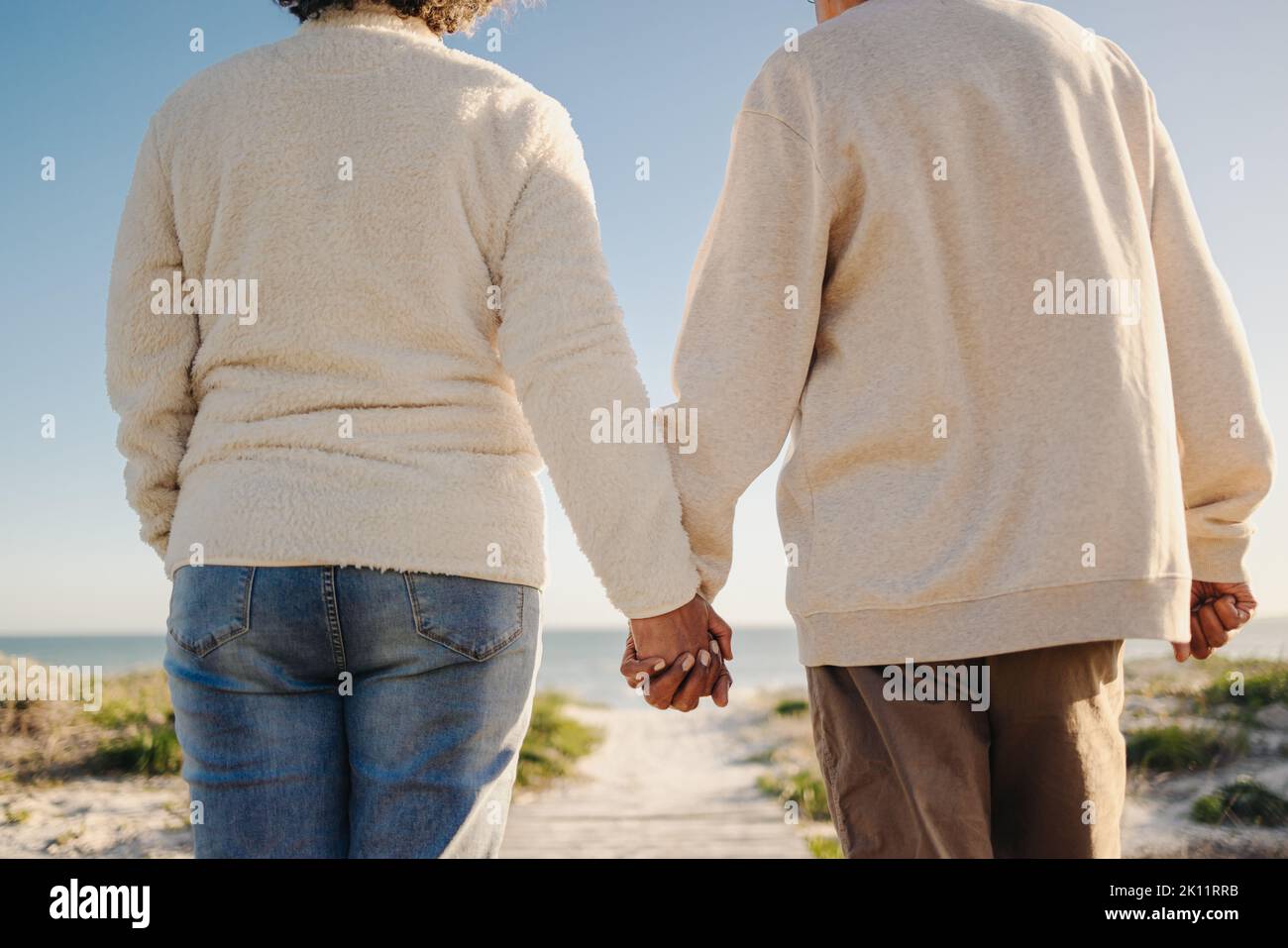 Una pareja mayor de la mano mientras camina por un puente peatonal en la playa. Una pareja de ancianos irreconocible disfrutando de unas refrescantes vacaciones junto al mar después de comer Foto de stock