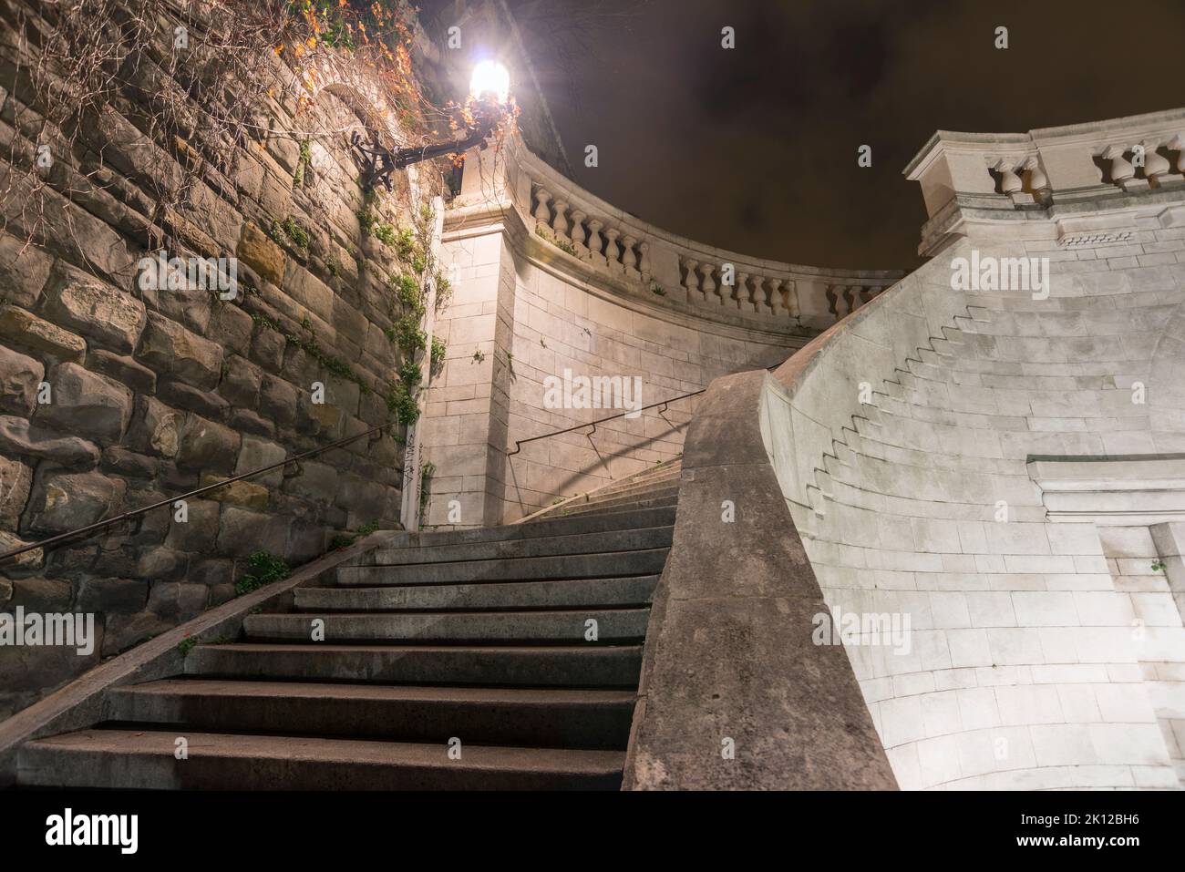Enormes escalones de piedra de escaleras serpenteantes iluminadas por la noche en la ciudad de Trieste, Italia Foto de stock