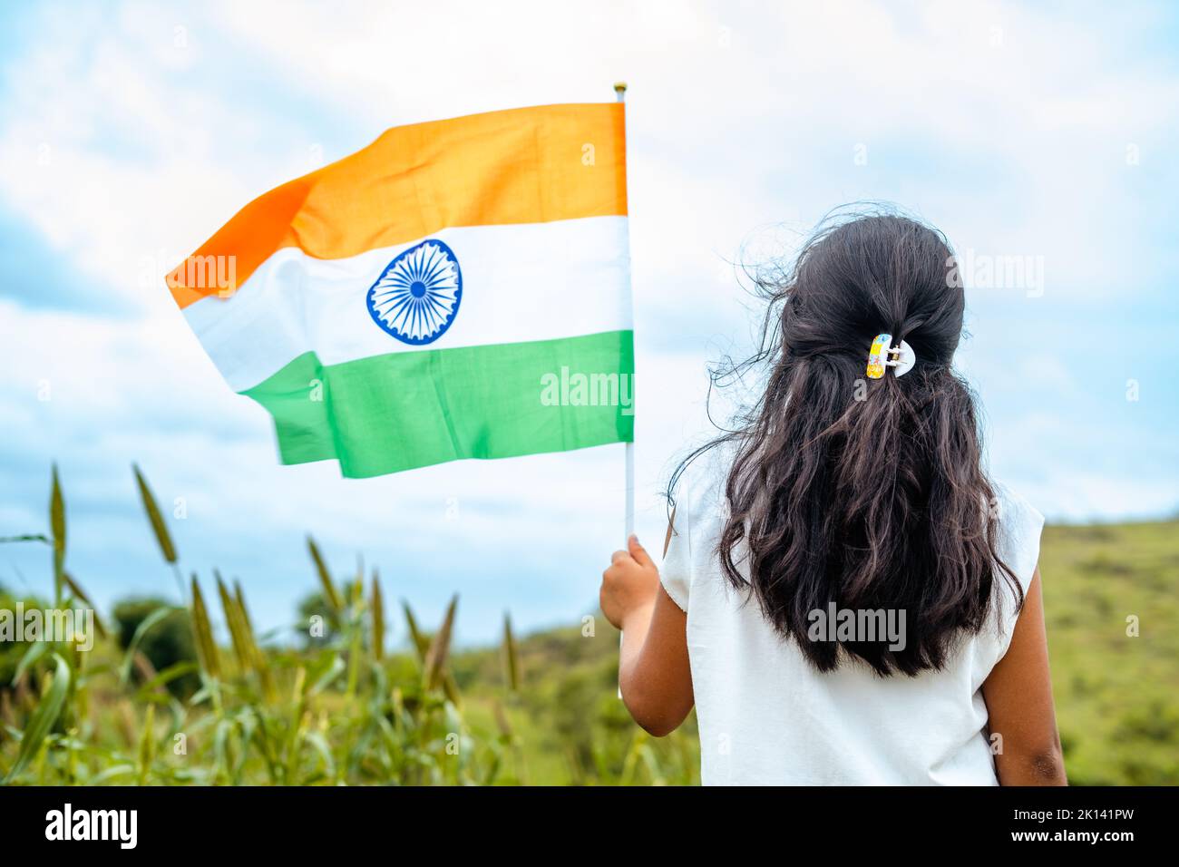 Vista trasera de una niña corriendo con una bandera india ondeando en la mano - concepto de patriotismo, celebración del día de la república y libertad Foto de stock