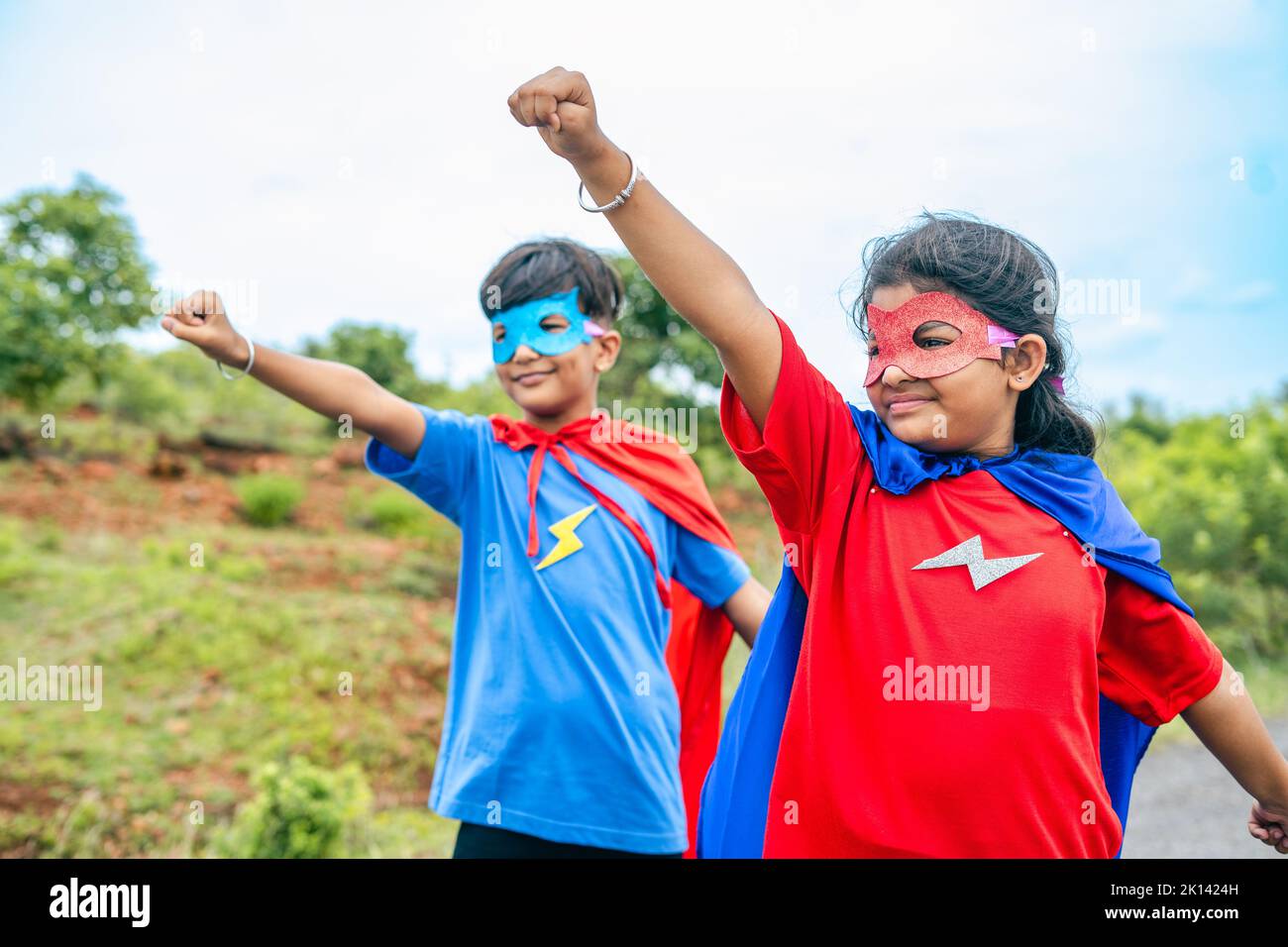 emocionados niños adolescentes felices disfraces de superhéroe en la carretera vacía con gesto de vuelo - concepto de fantasía, trabajo en equipo y coraje. Foto de stock