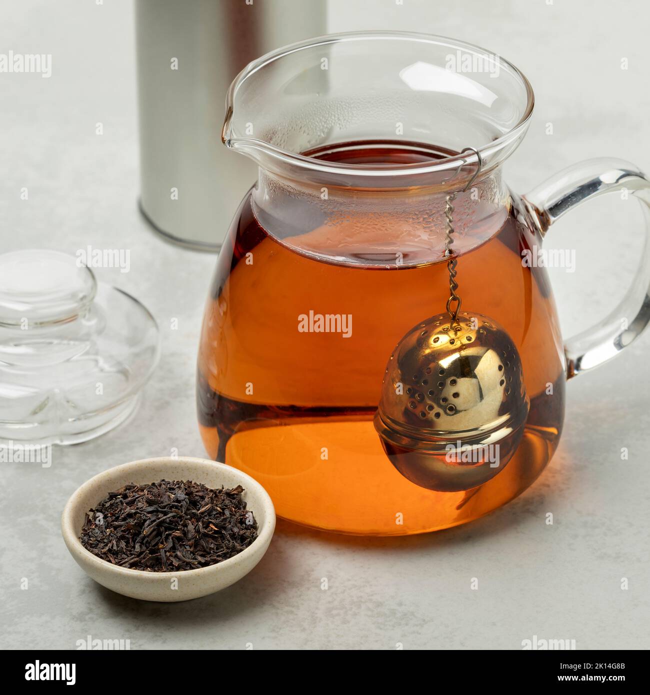 Tetera de cristal con un infusor de té de metal y un tazón con té Ostfriesen alemán en frente Foto de stock