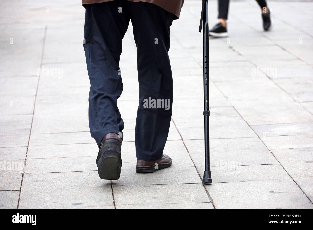 Anciano caminando con un bastón por la calle de la ciudad. Enfermedades de la columna vertebral y las piernas de los ancianos Foto de stock