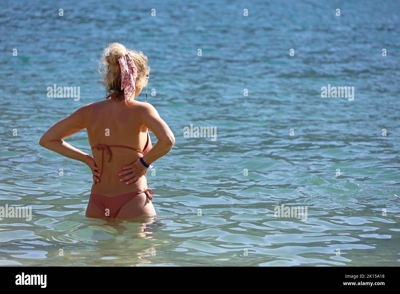 Mujer delgada en bikini de pie en el agua del mar y mirando a la distancia. Vacaciones en una playa de complejo soleado Foto de stock