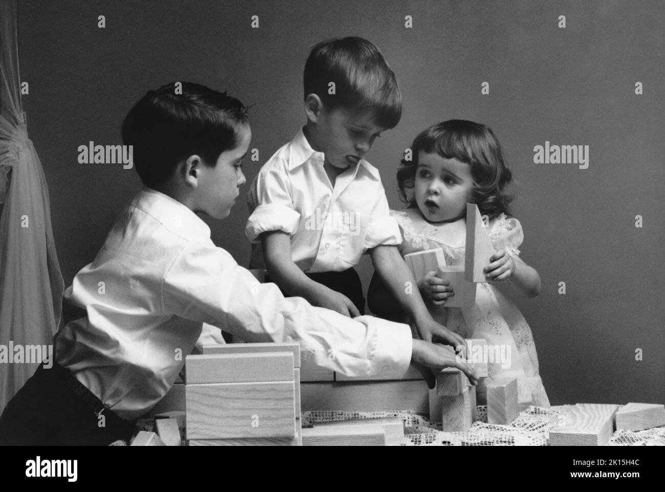 Los hermanos juegan bloques con su hermana pequeña; NYC, 1955. Foto de stock