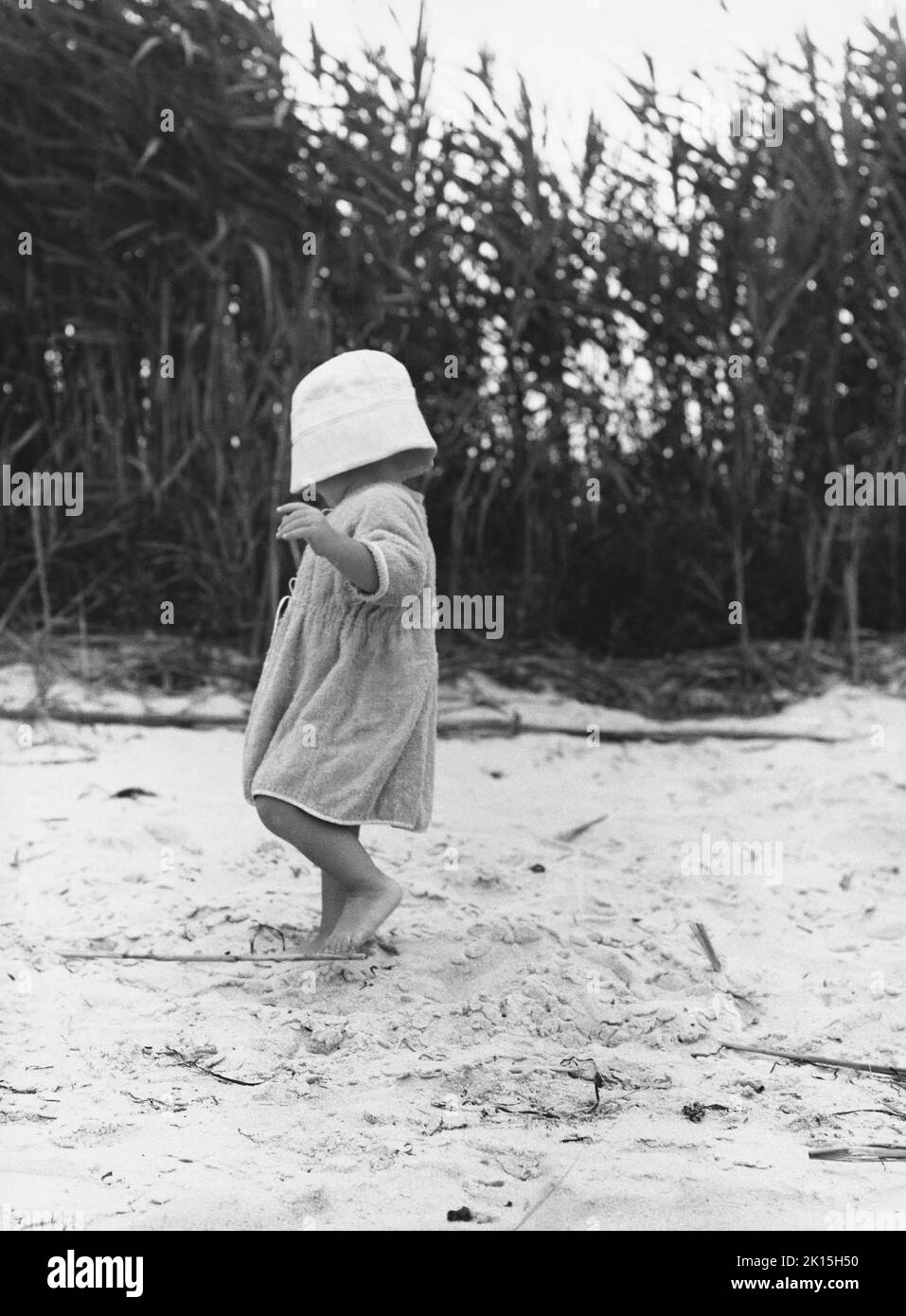 Una niña con un sombrero tirado sobre sus ojos camina descalzo en la playa. Foto de stock