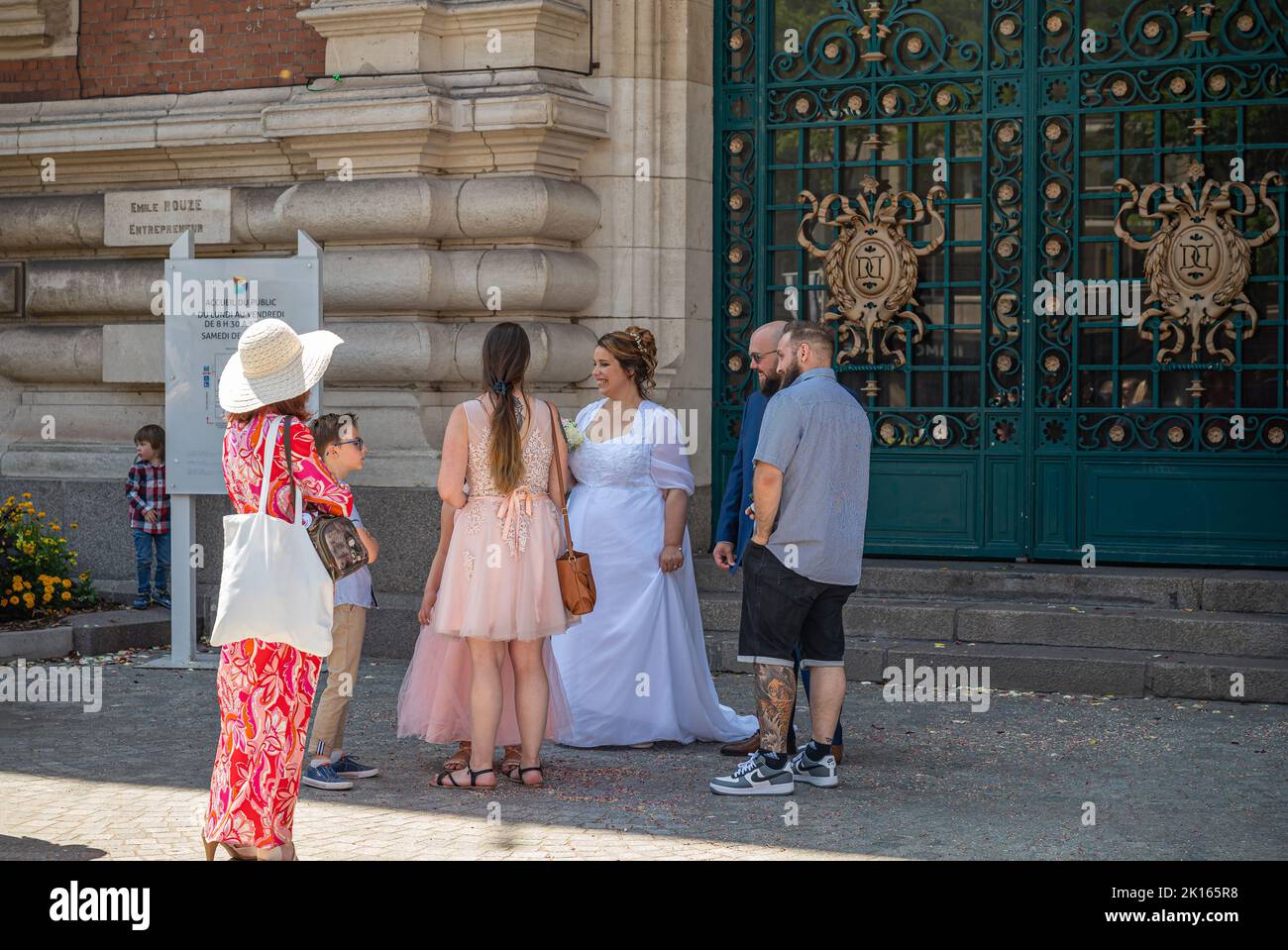 Europa, Francia, Dunkerque - 9 de julio de 2022: Pequeño grupo de personas se reúnen alrededor de la novia en blanco a la espera de la llegada del novio delante de la entrada principal a. Foto de stock