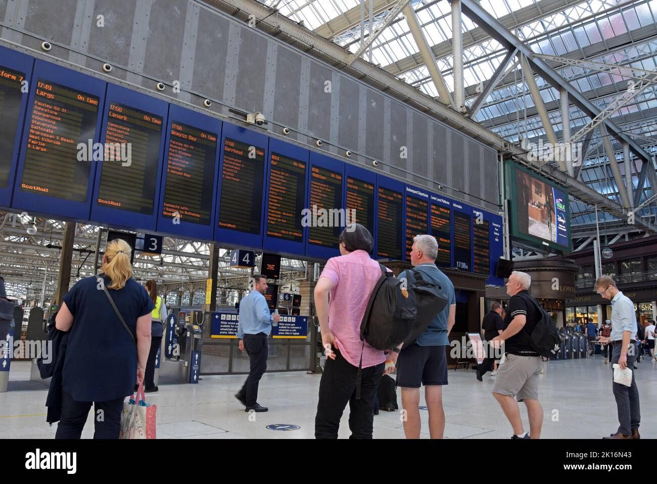 Los pasajeros que esperan trenes observan las tablas de salidas en la estación central de Glasgow, Escocia, Reino Unido Foto de stock