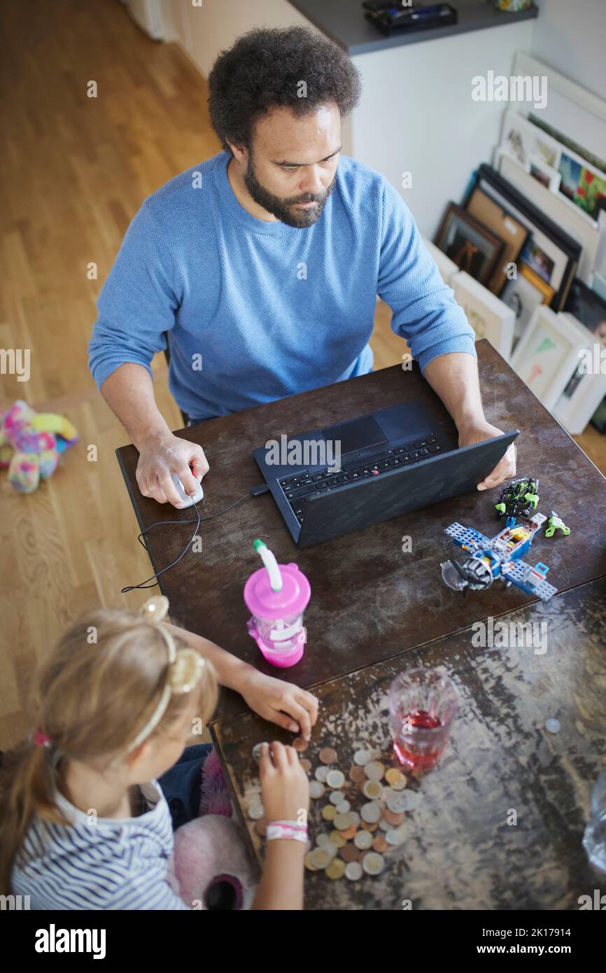 Hombre trabajando desde casa mientras hija cuenta ahorros Foto de stock
