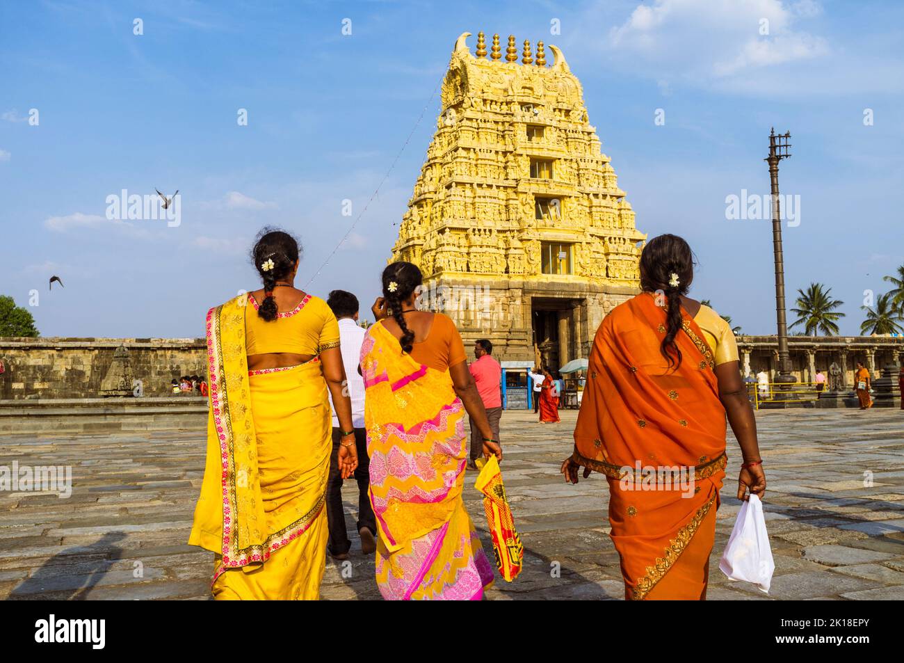 Belur, Karnataka, India : Tres mujeres en saris coloridos caminan hacia la puerta gopuram del templo Channakeshava del siglo 12th. Foto de stock