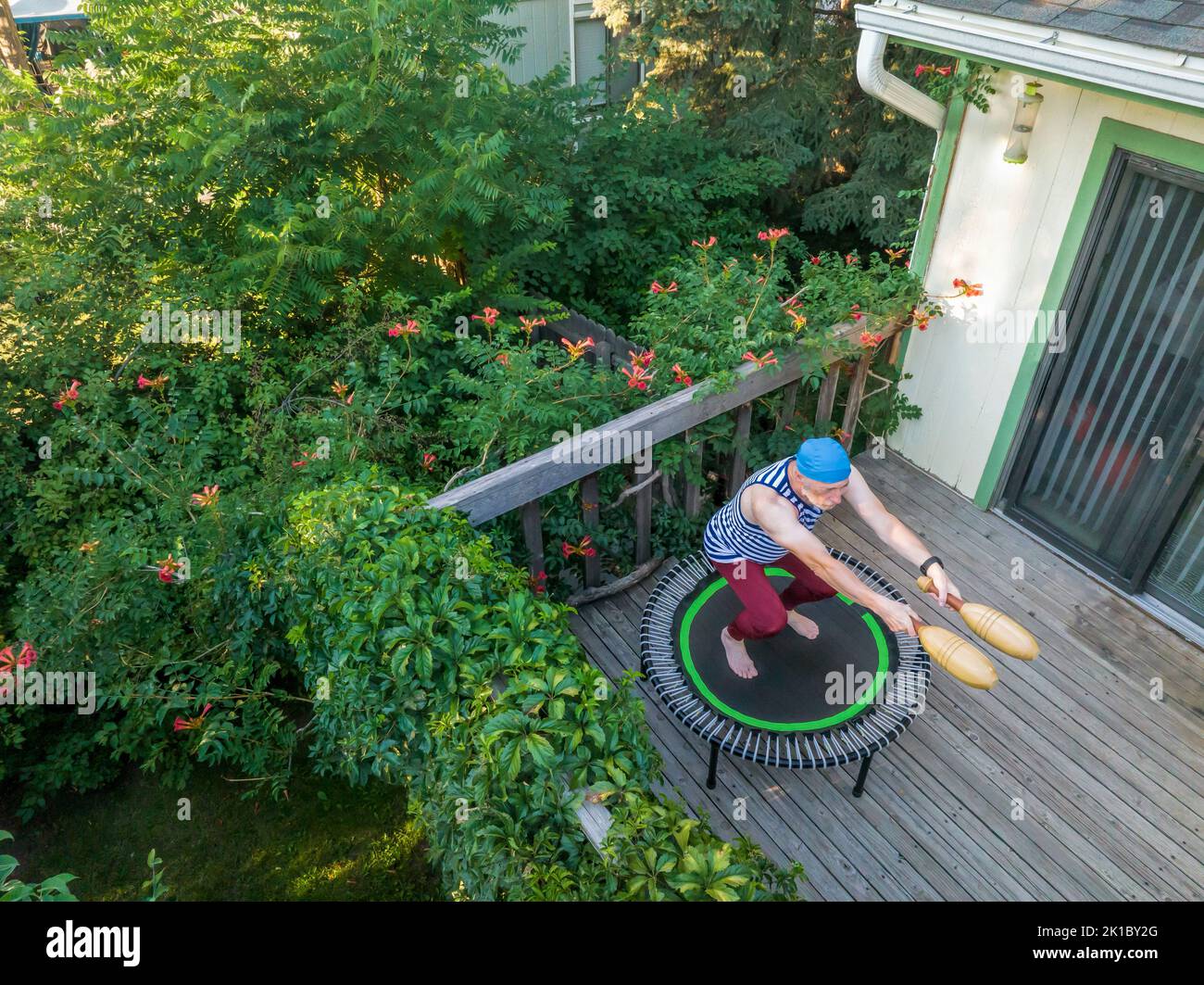El hombre mayor está rebotando en un mini trampolín con palos indios de madera en su patio trasero, vista aérea de finales de verano en Colorado Foto de stock