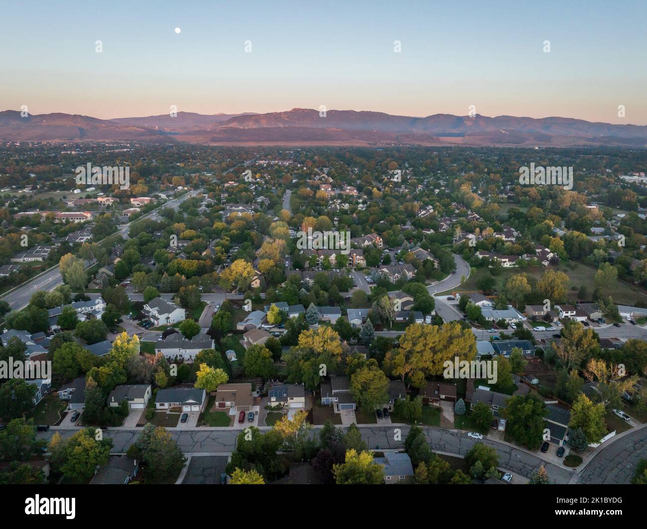Amanecer de verano con luna llena sobre la zona residencial de Fort Collins y las estribaciones de las Montañas Rocosas en el norte de Colorado, vista aérea Foto de stock