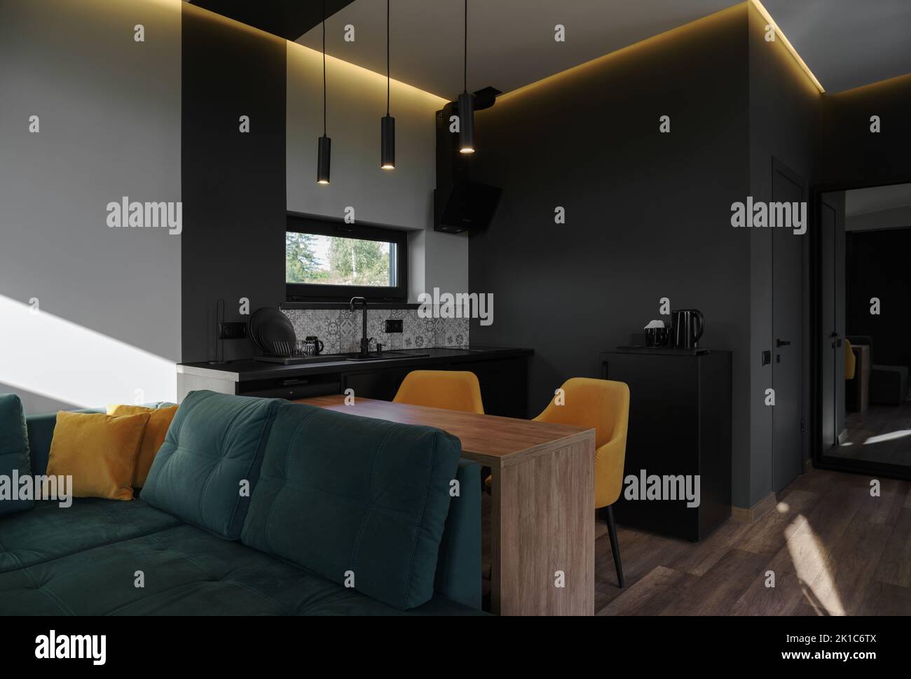 Este moderno apartamento estudio cuenta con sofá verde y sillas amarillas en la cocina oscura con espacio para copiar Foto de stock
