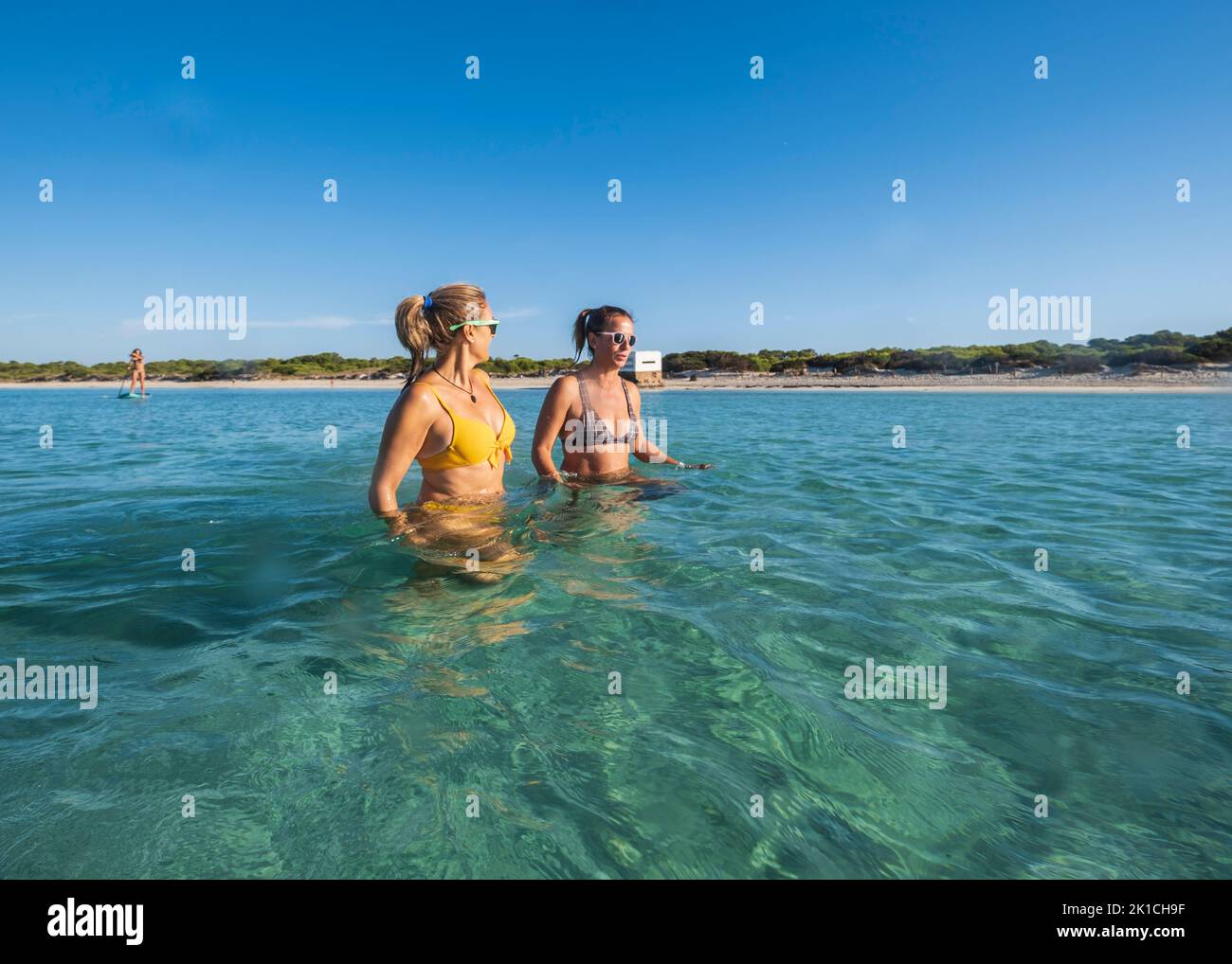 Dos mujeres adultas hablando mientras caminan por el agua, playa de Ses Covetes, Mallorca, Islas Baleares, España Foto de stock