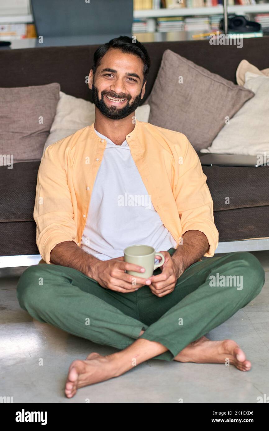 Hombre indio feliz mirando la cámara de beber café en casa. Vertical Foto de stock