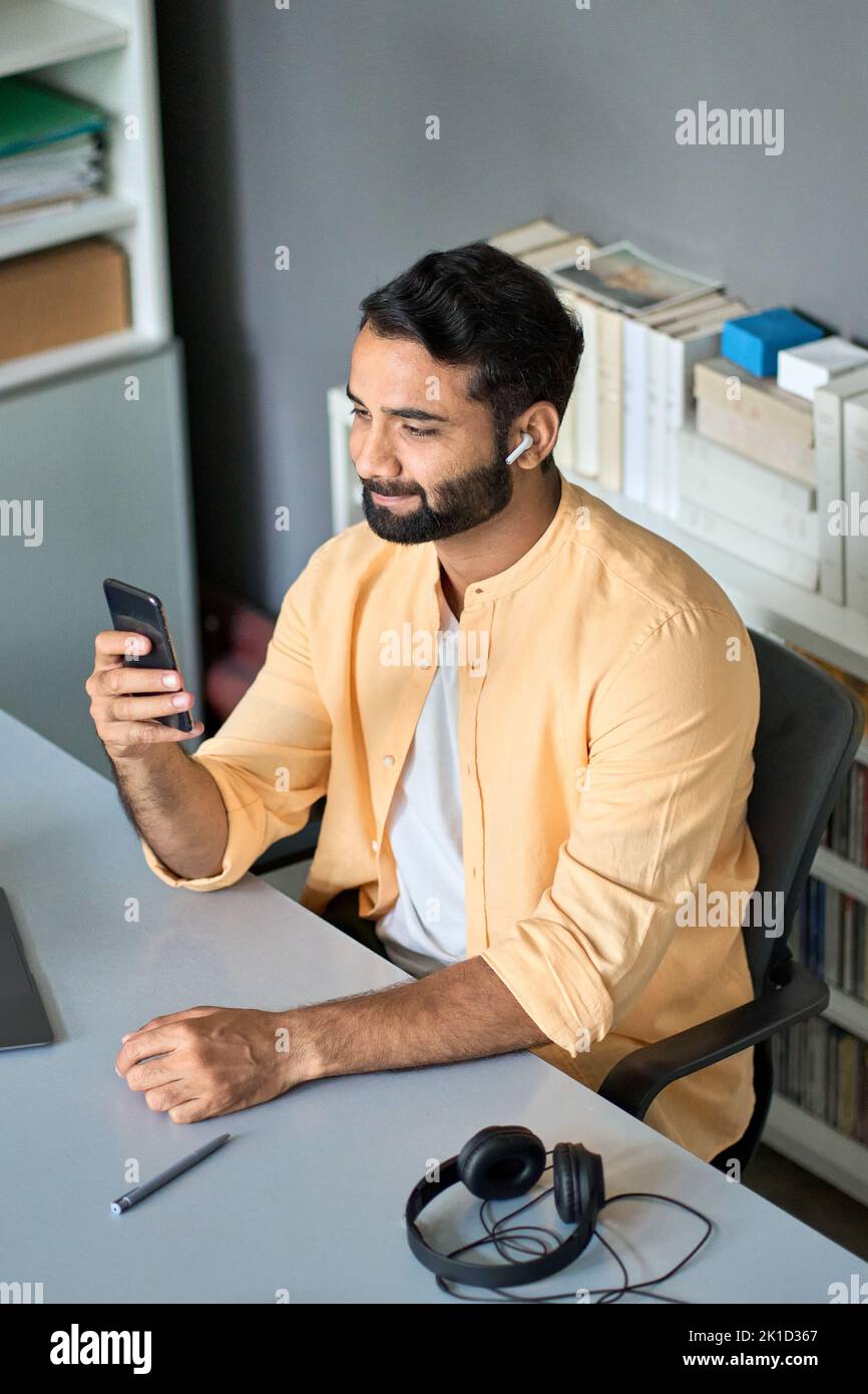 Hombre de negocios indio teniendo videollamada en el trabajo utilizando el teléfono móvil, vertical. Foto de stock