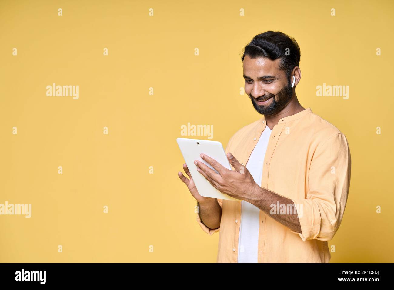 Hombre indio feliz utilizando la tableta digital aislado sobre fondo amarillo. Foto de stock
