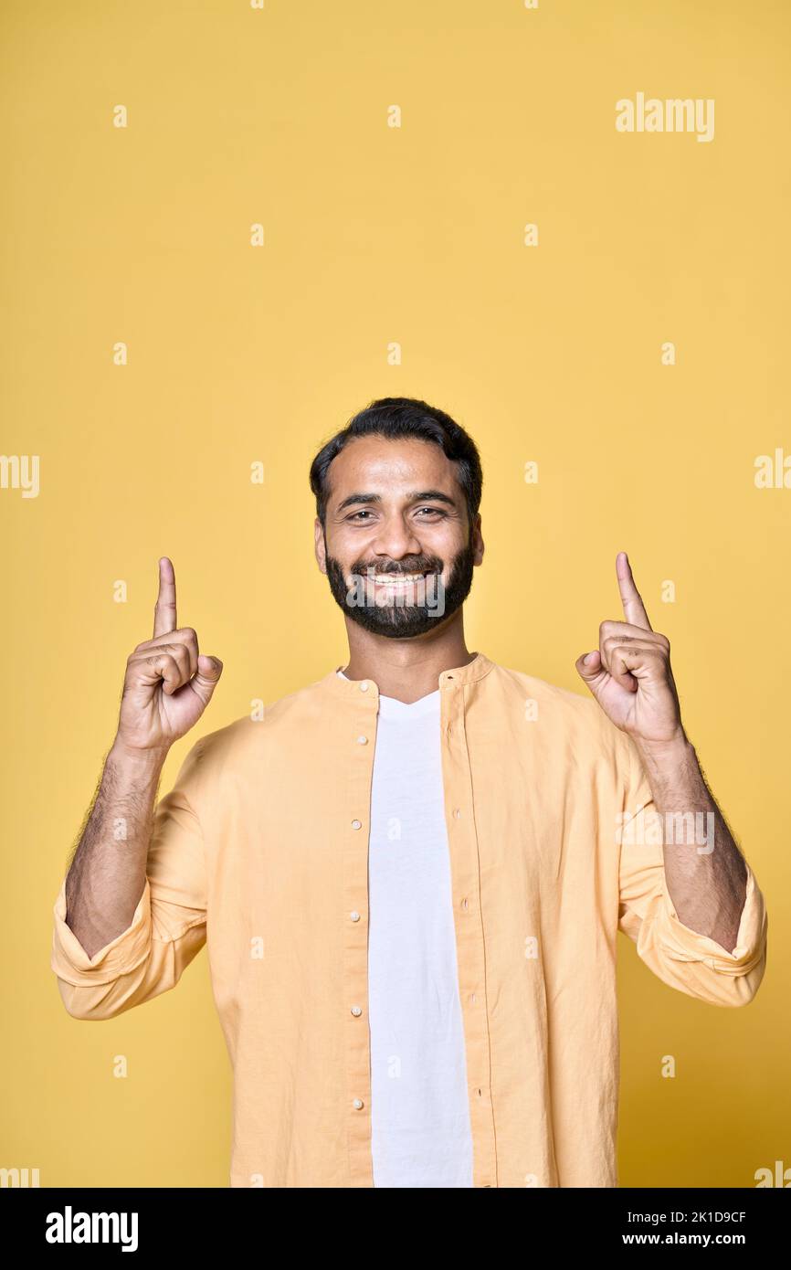 Hombre indio feliz señalando con los dedos la publicidad aislada sobre fondo amarillo. Foto de stock