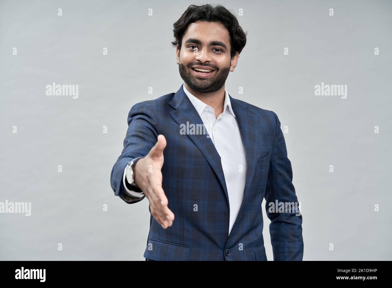 Sonriente hombre de negocios árabe extendiendo la mano para apretón de manos aislado en beige. Foto de stock