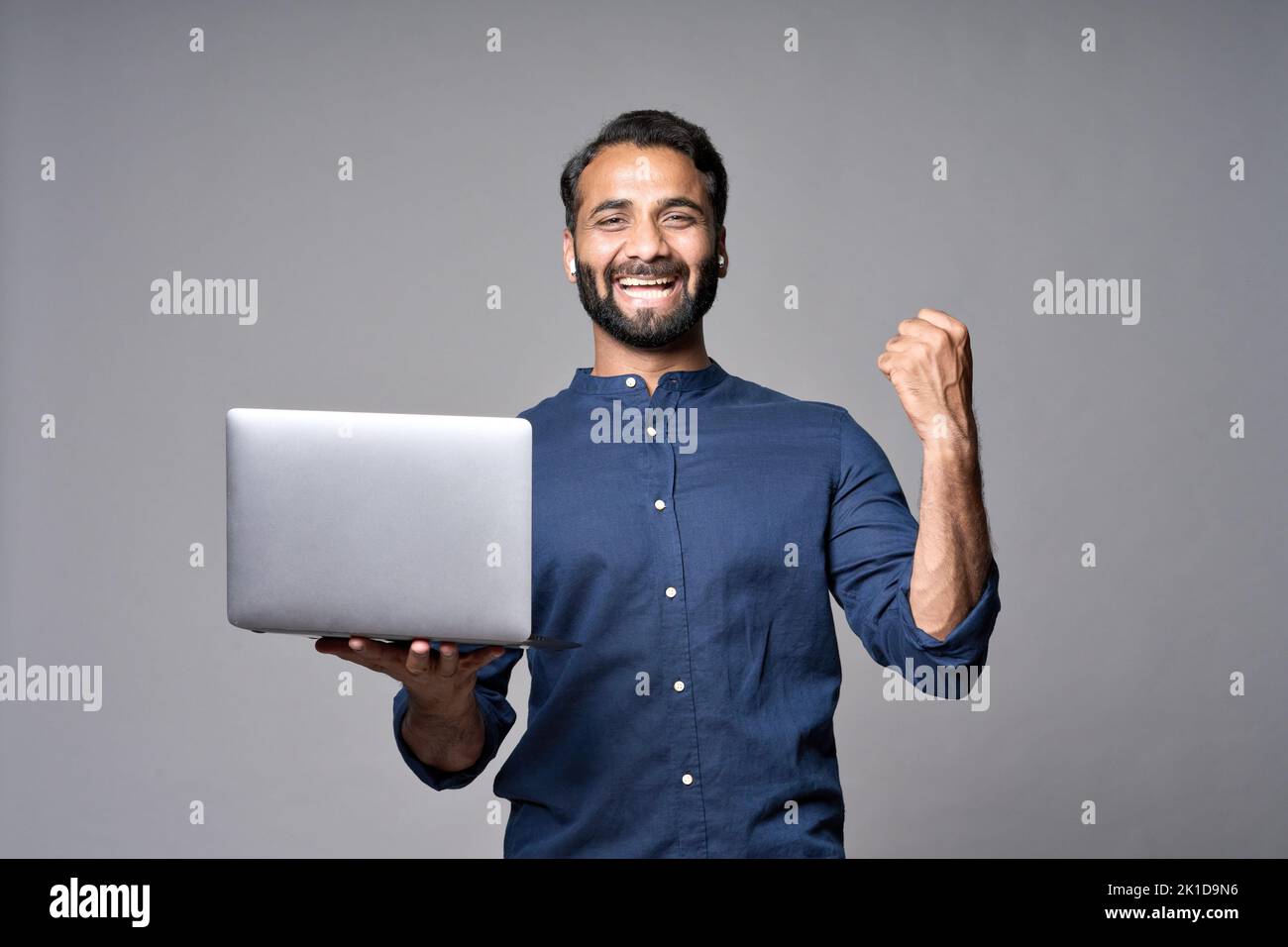 Feliz hombre de negocios indio con portátil aislado en gris celebrando el resultado. Foto de stock