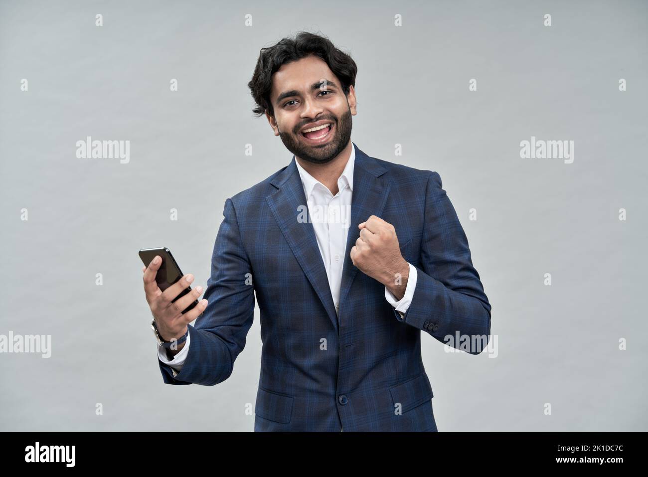 Feliz hombre de negocios indio sosteniendo teléfono celular celebrando el triunfo aislado en beige. Foto de stock