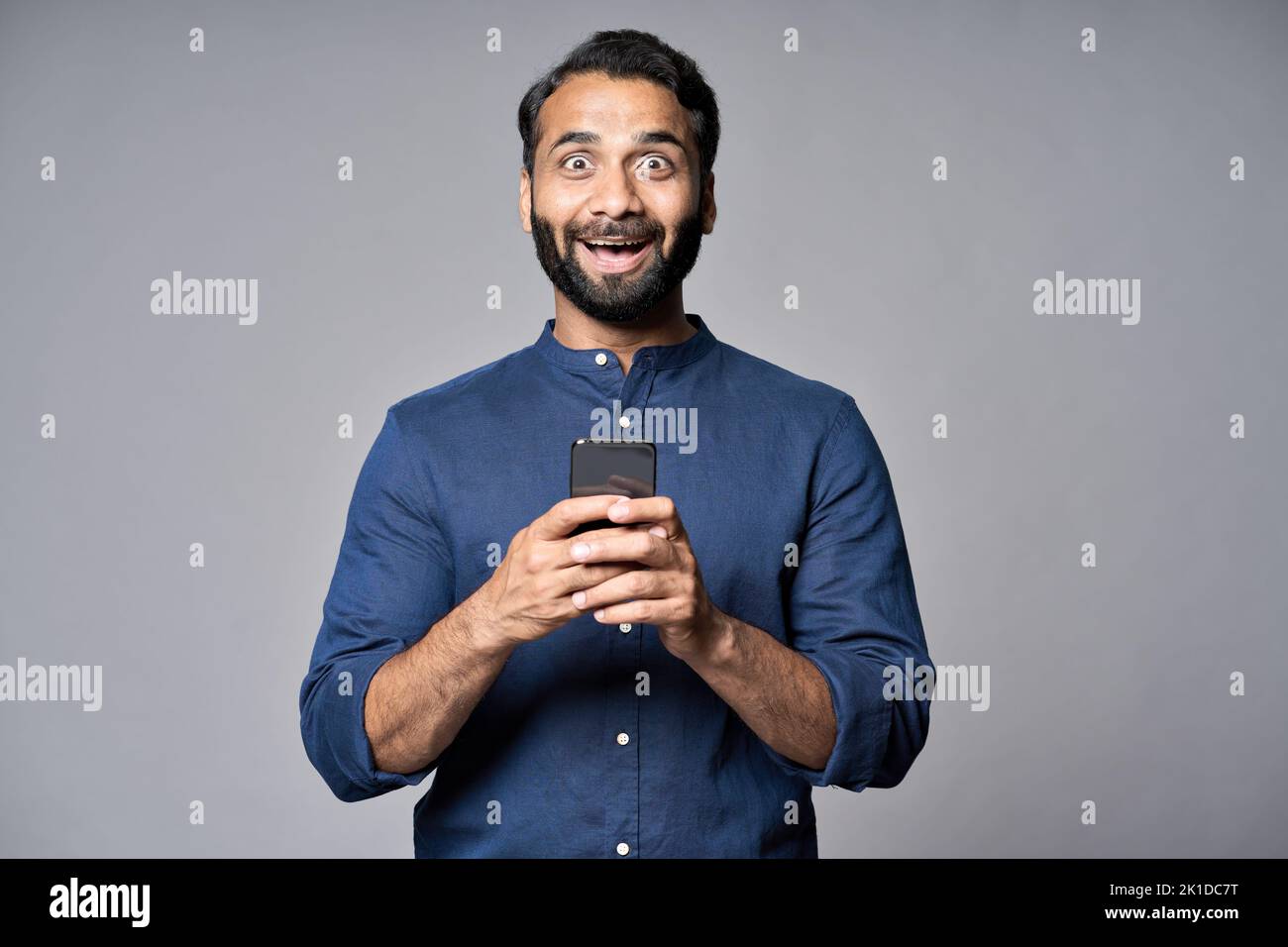 Entusiasmado hombre de negocios indio utilizando teléfono móvil aislado sobre fondo gris. Foto de stock
