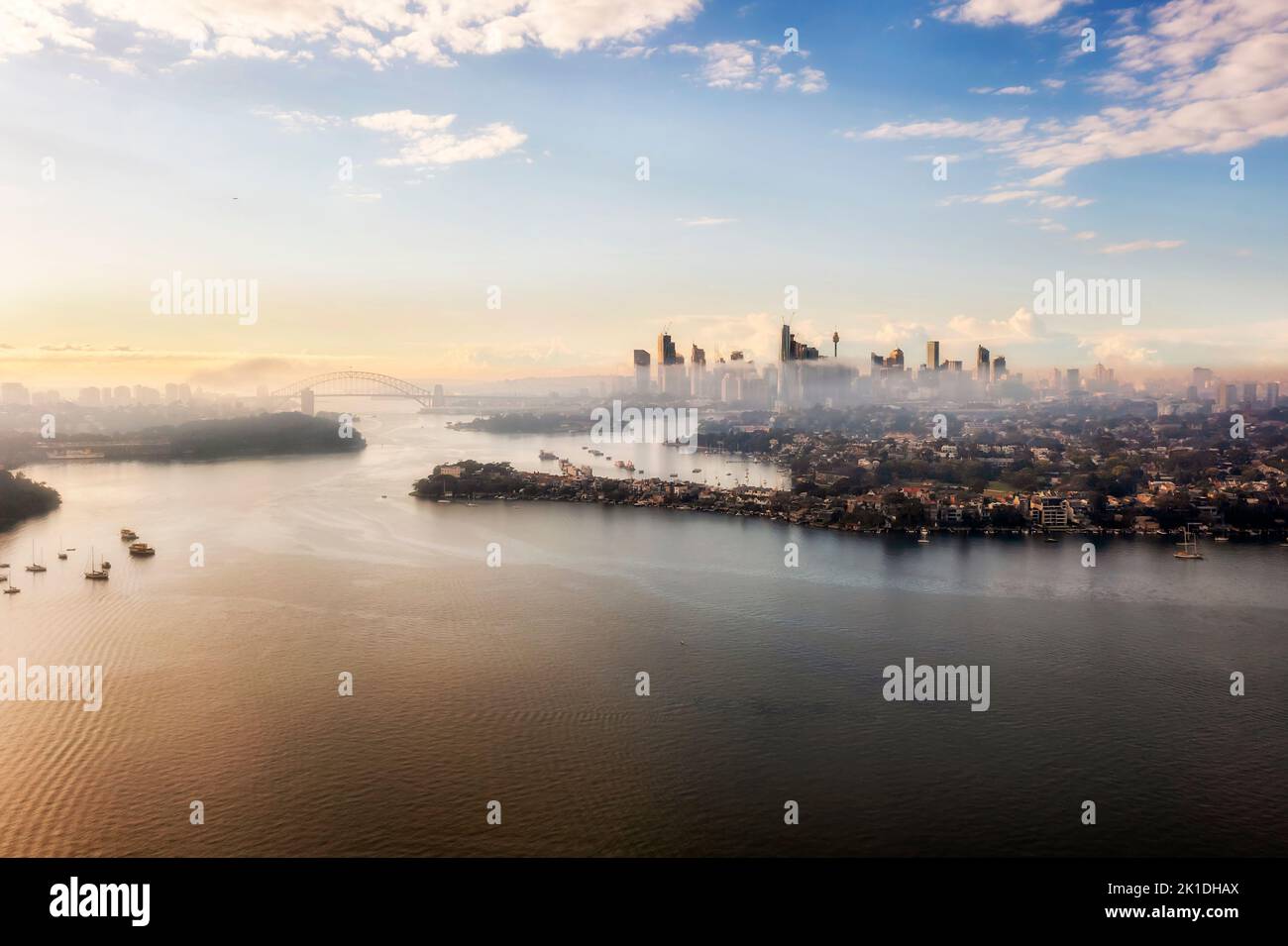 Paisaje urbano aéreo del río Parramatta en el puerto de Sídney y monumentos arquitectónicos del distrito central de negocios en el horizonte con un tiempo nublado al amanecer. Foto de stock