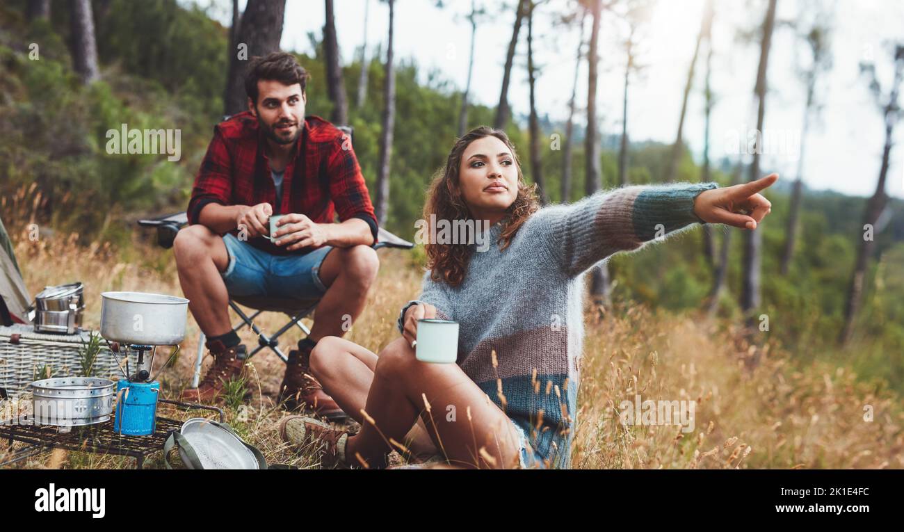 Mujer joven señalando una dirección mientras acampaba con su novio. Pareja joven aventurera disfrutando de sus vacaciones en un camping. Foto de stock