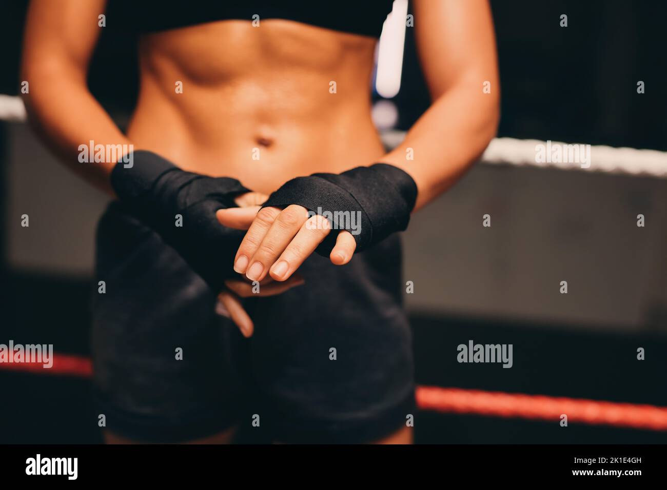 Boxer femenino envolver sus manos mientras está de pie en un ring de boxeo. Mujer joven atlética preparándose para una sesión de entrenamiento de boxeo en un gimnasio de fitness. Foto de stock