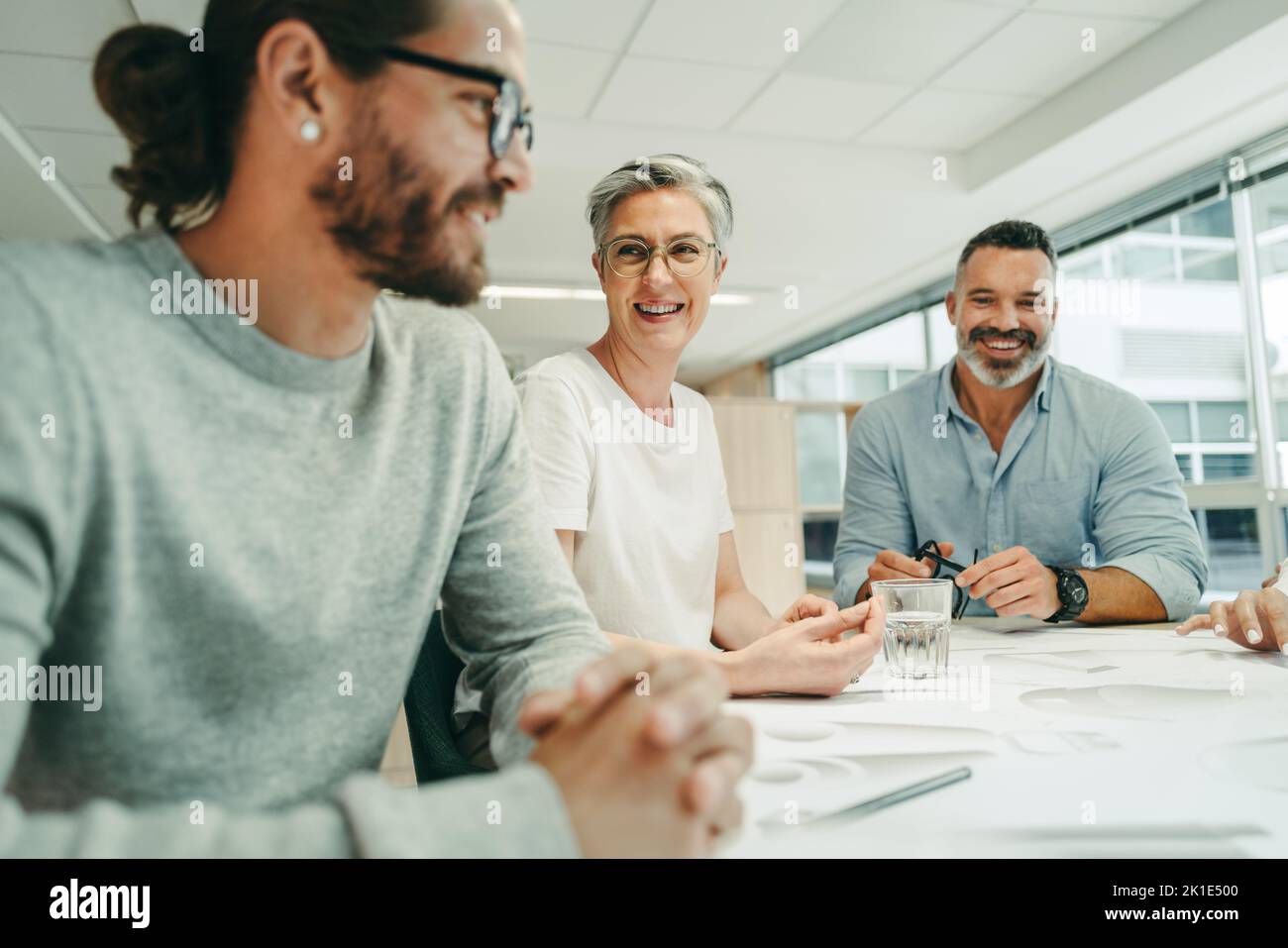 Arquitectos alegres sonriendo alegremente durante una reunión en una oficina moderna. Grupo de empresarios innovadores que trabajan con blueprints. Bu. Creativo Foto de stock