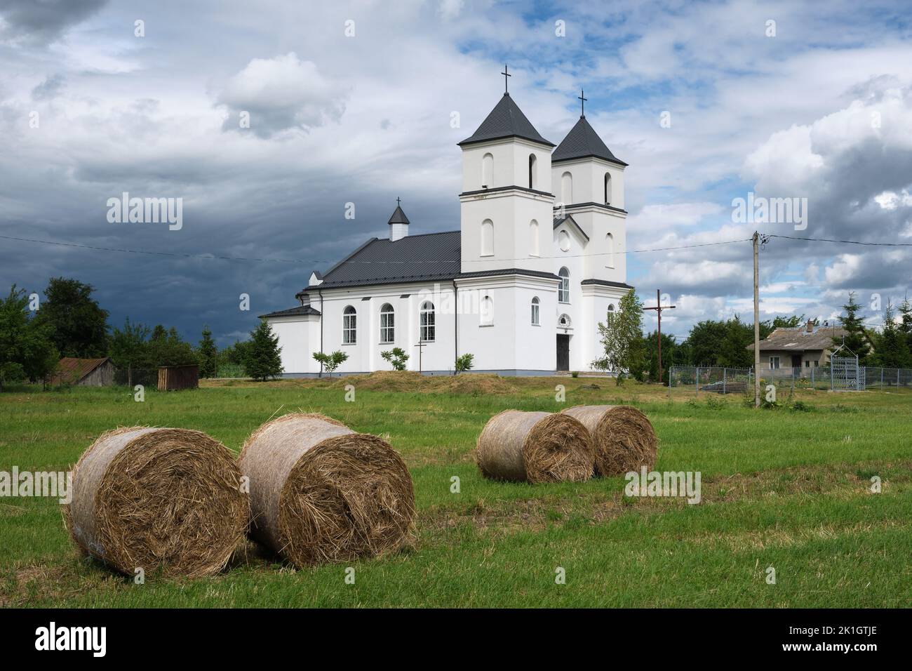 Vista de la antigua iglesia católica de la Trinidad y pilas de heno en el campo, pueblo Yushkovichi, distrito Baranovichi, región de Brest, Bielorrusia. Foto de stock