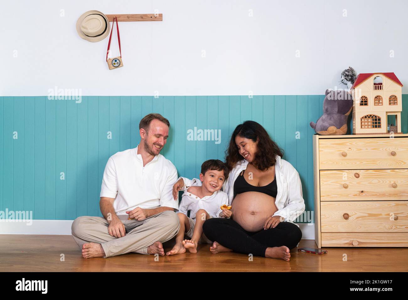 Foto de joven alegre pareja positiva sonriente esposa embarazada y marido con su hijo en casa Foto de stock