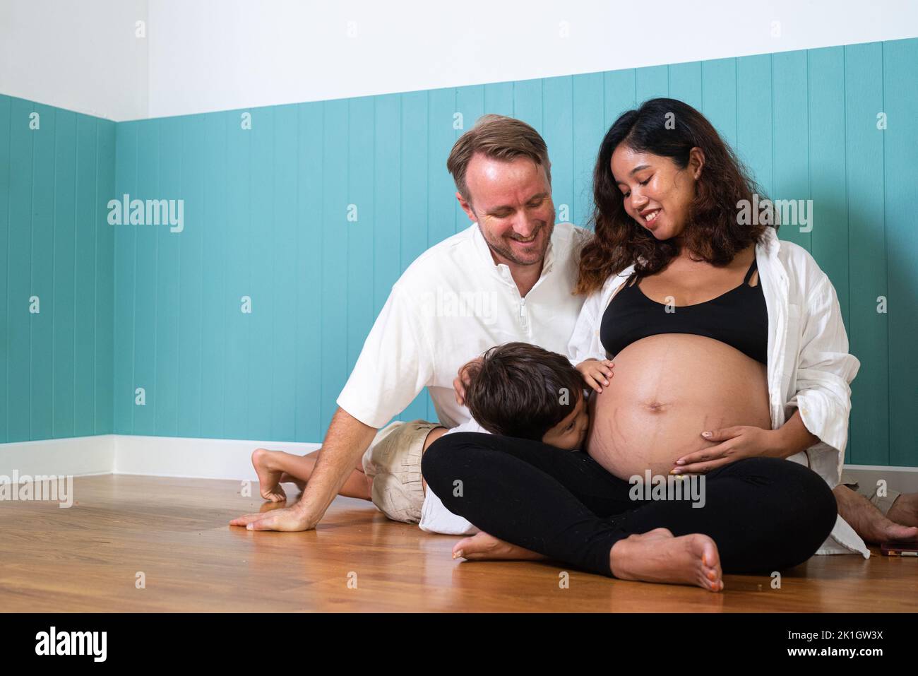 Foto de joven alegre pareja positiva sonriente esposa embarazada y marido con su hijo en casa Foto de stock