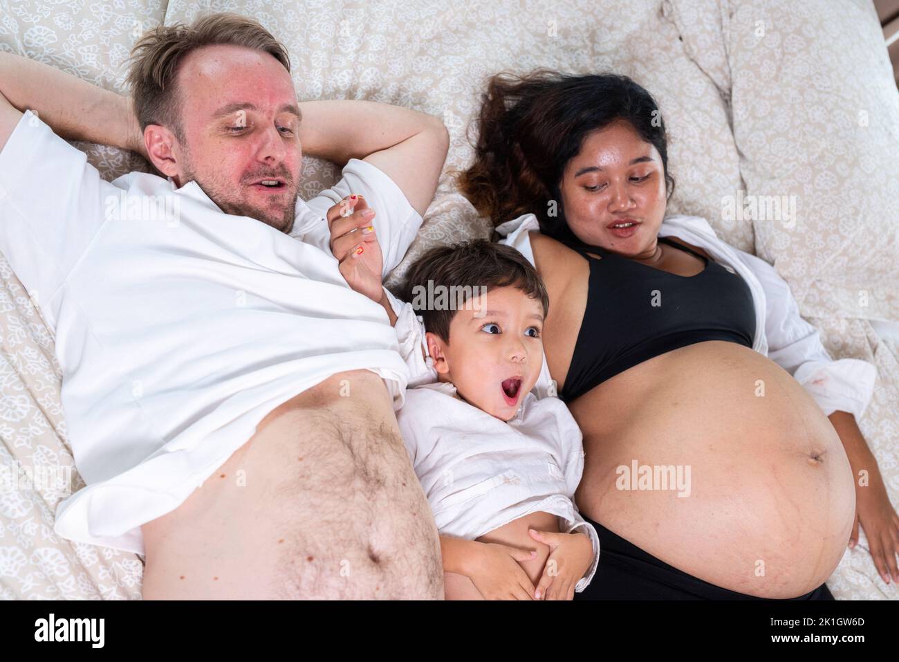 Foto de joven alegre pareja positiva sonriente esposa embarazada y marido con su hijo relajándose en casa Foto de stock