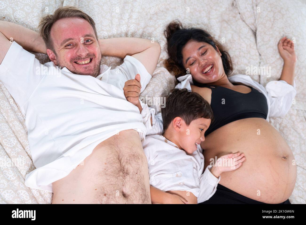 Foto de joven alegre pareja positiva sonriente esposa embarazada y marido con su hijo relajándose en casa Foto de stock