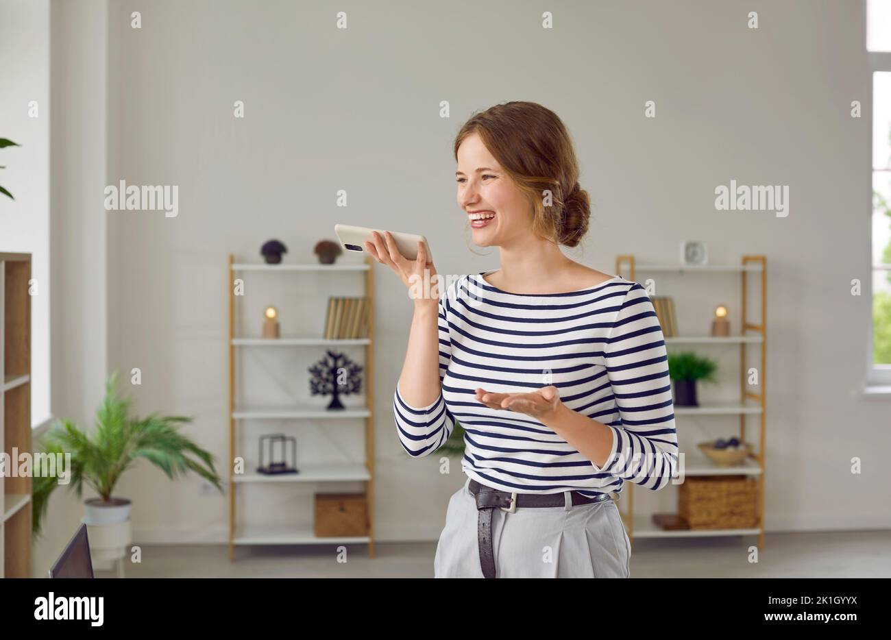 Una mujer sonriente y alegre responde a la llamada entrante o deja un mensaje de audio de voz de forma remota. Foto de stock