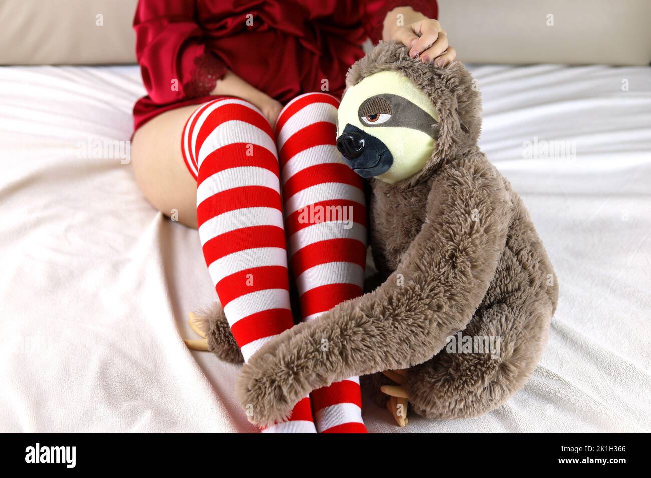 Mujer sexy en Navidad calcetines rodilla con pereza juguete sentado en la cama. Regalo de vacaciones, chica sola, concepto de celebración o soledad Foto de stock