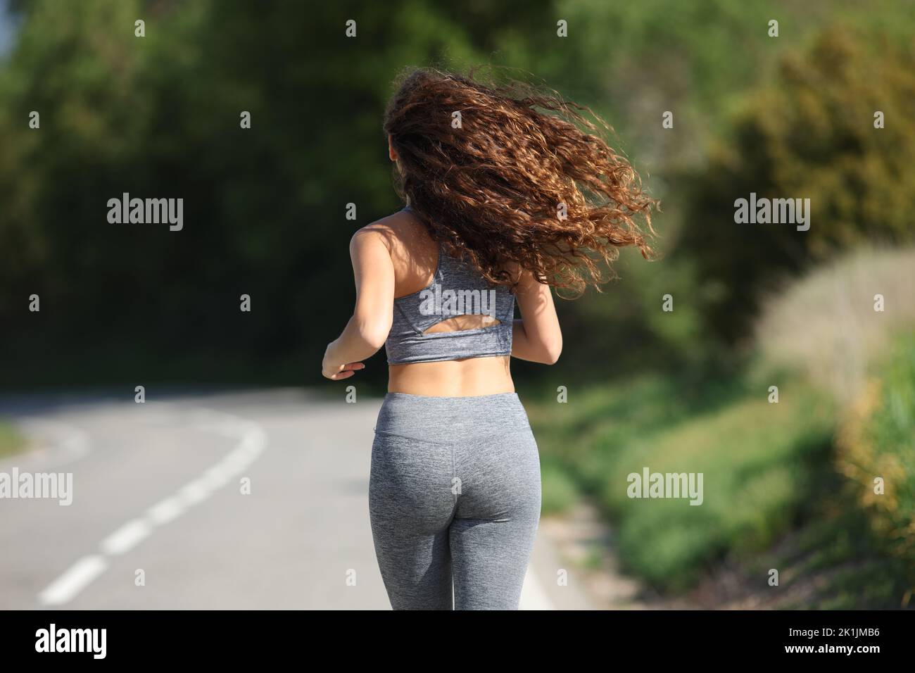 Vista posterior retrato de una mujer corriendo en una carretera Foto de stock