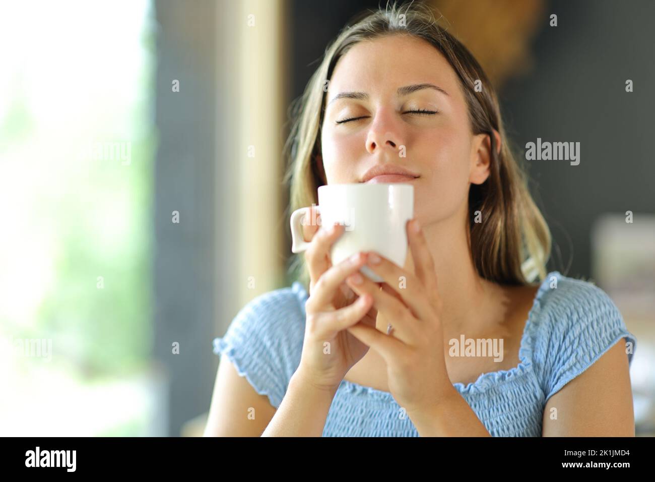 Mujer joven oliendo el aroma del café de una taza en un restaurante Foto de stock