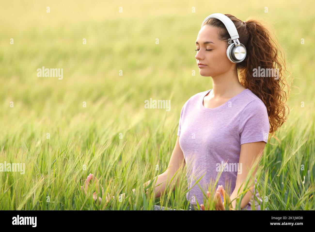 Mujer concentrada usando auriculares haciendo meditación de yoga con tutorial en línea en un campo Foto de stock