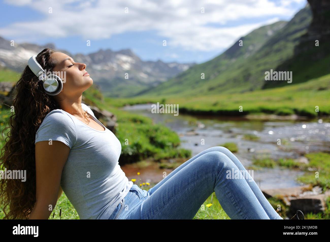 Retrato lateral de una mujer que se relaja escuchando música con auriculares en la naturaleza Foto de stock