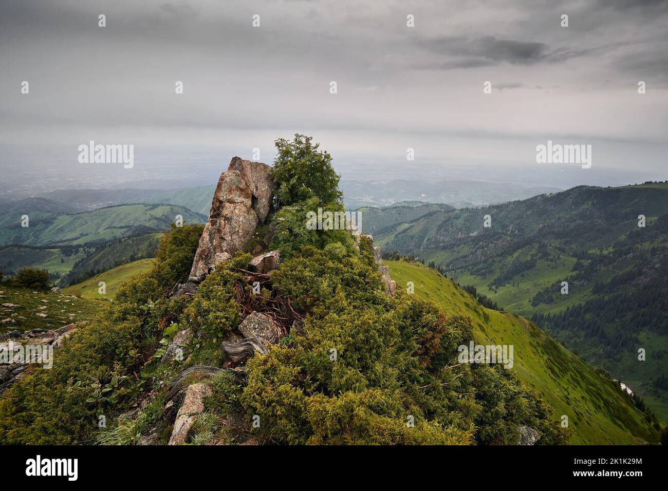 Hermoso paisaje de cumbre rocosa en las verdes colinas en el valle de la montaña y verde prado exuberante en el cielo oscuro de la tormenta y la lluvia en Almaty, Kazajstán Foto de stock