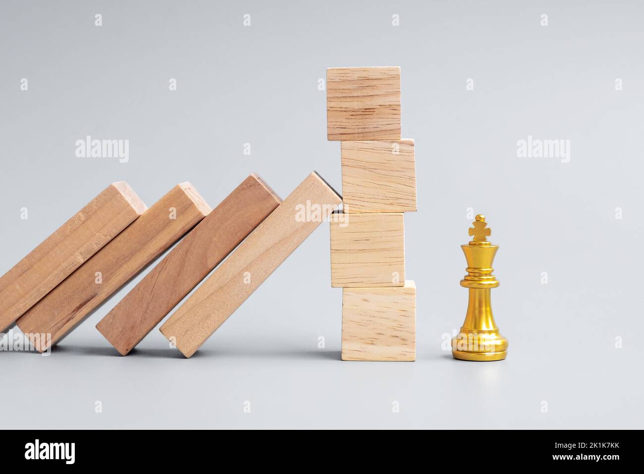 Bloques de madera o dominó cayendo a la figura de rey de ajedrez dorado. Negocio, Gestión de riesgos, Solución, Regresión económica, Seguros Foto de stock