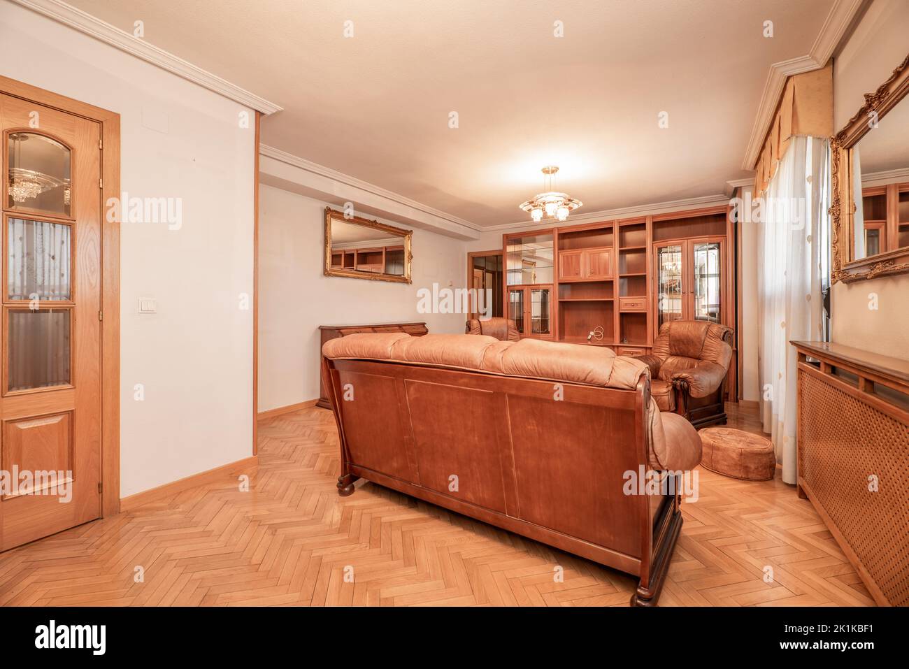 Sala de estar amueblada con sofás de madera de época, suelos de parqué de roble francés y estantería en la pared Foto de stock